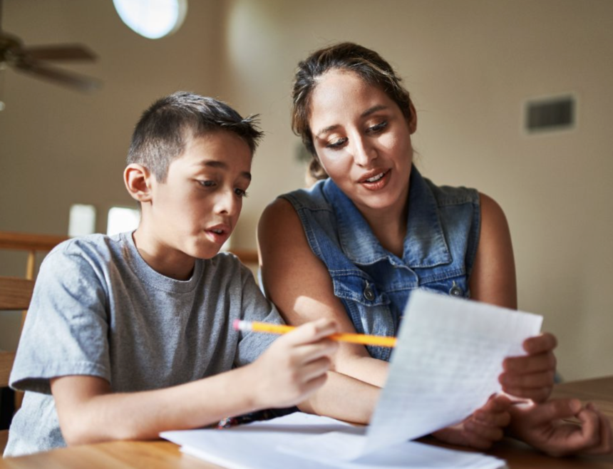 mother teaching her don to read while holding the paper.